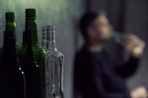 man drinking near already empty bottles showing symptoms of alcohol poisoning