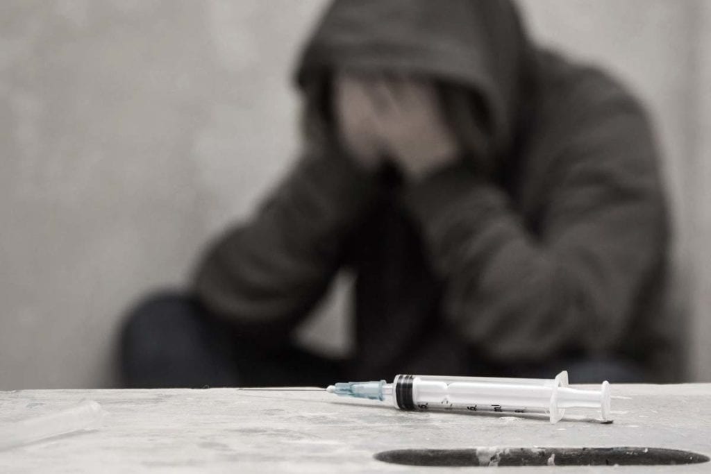 A man sits on a curb and wonders if he needs a heroin addiction treatment center