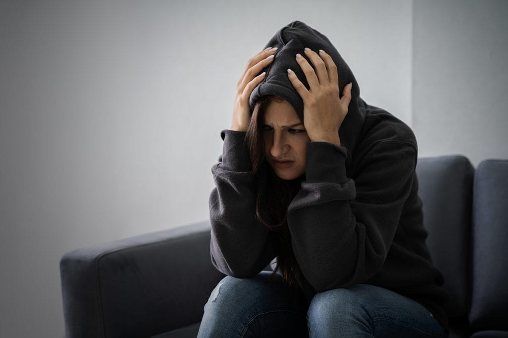 man in hoodie holding head coping with opioid withdrawal