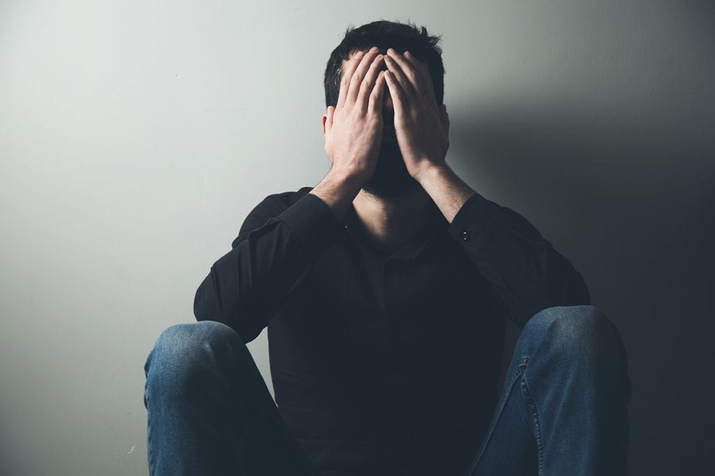 man slumped against wall with hands to face worried about long term effects of alcohol