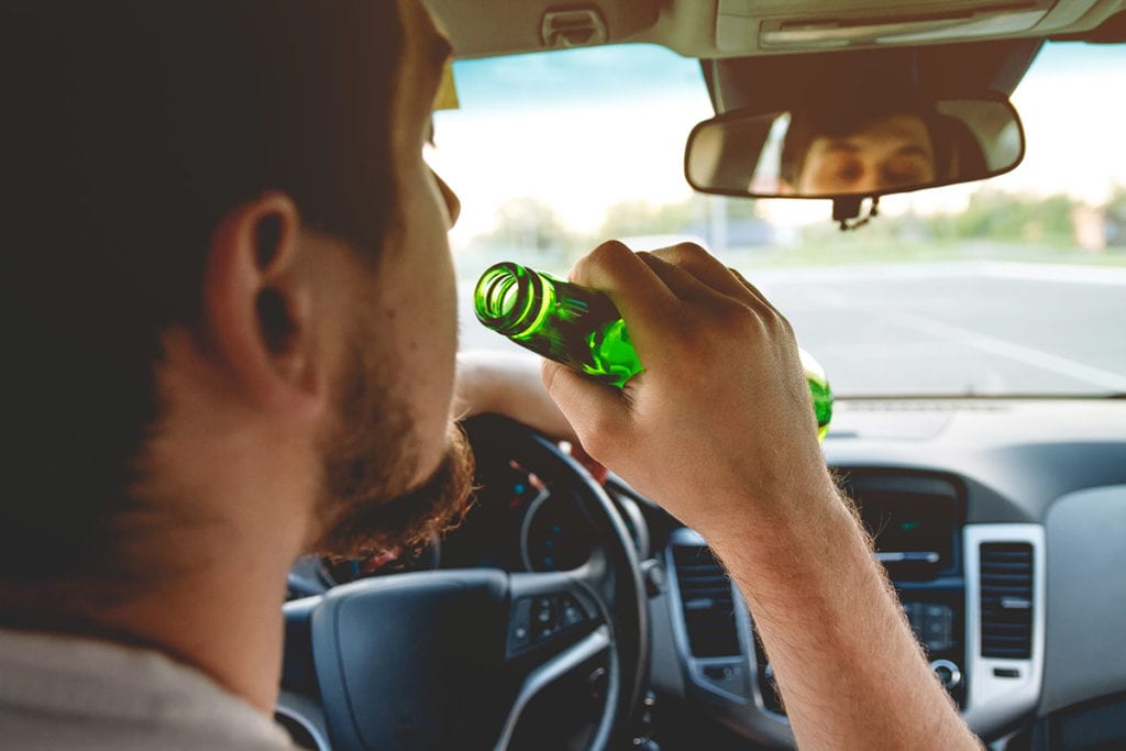 man with a beer bottle behind the wheel drinking and driving