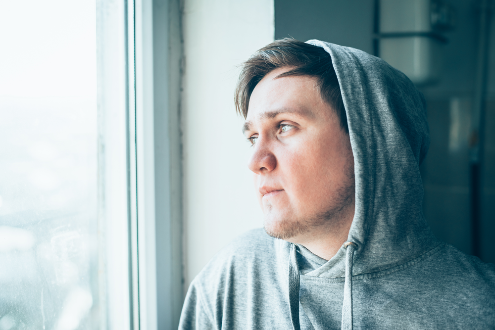 man looking out window thinking about drug abuse vs drug addiction
