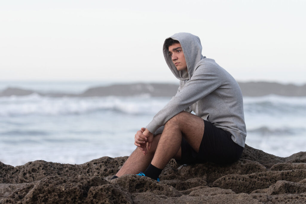 Person sitting next to the shore and wondering about the signs of PCP addiction