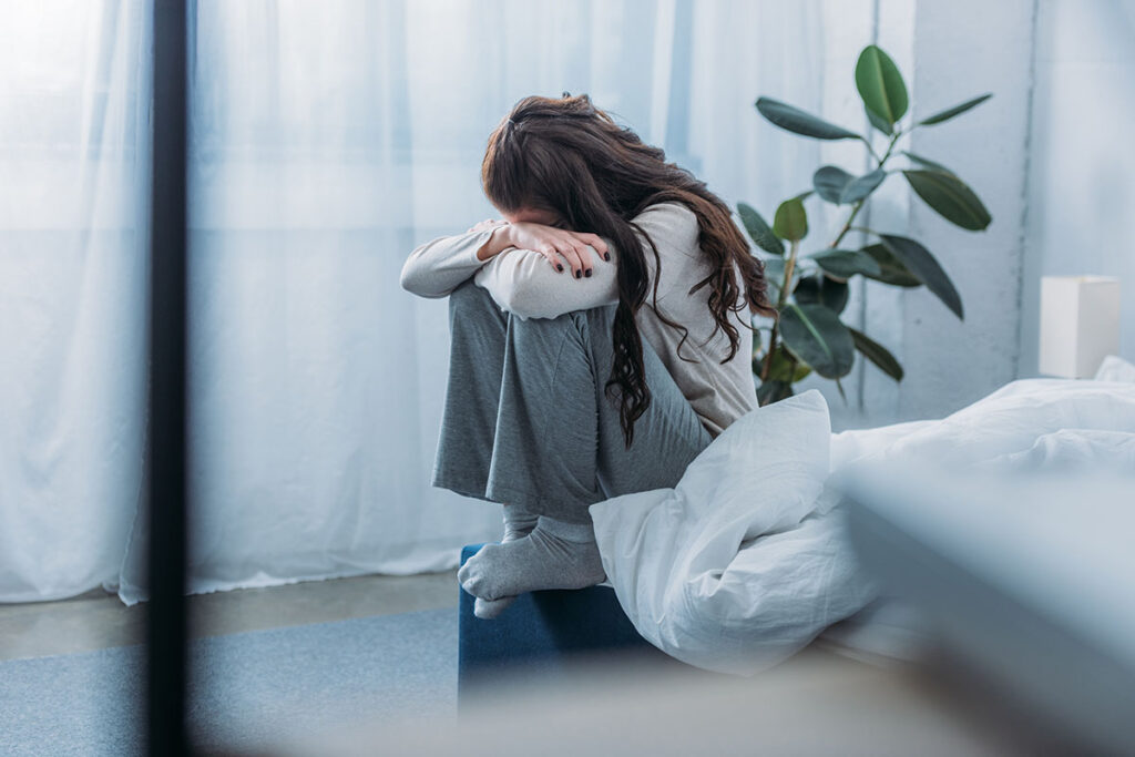 Person sitting on the ground next to window, experiencing the effects of consuming alcohol and anxiety symptoms